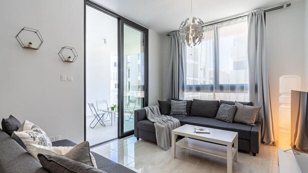 A modern living room with a grey sofa, a white coffee table, and a balcony with a glass door. - Lana 1-Bedroom Apt & Balcony in Larnaca (Cyprus - Larnaca)