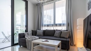 A modern living room with a dark grey sofa, a white coffee table, and a large window with sheer curtains. - Lana 1-Bedroom Apt & Balcony in Larnaca (Cyprus - Larnaca)