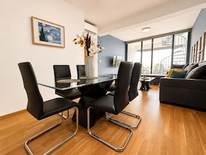 A modern living room with a glass dining table, black chairs, a sofa, and a large window.