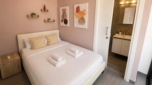 A bedroom with a bed, bedside tables, a nightstand, a bathroom with a sink, and a mirror. - Fiesta 1-Bedroom Apartment in Larnaca (Cyprus - Larnaca)