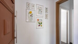 A hallway with framed botanical illustrations on the wall, a wooden door, and a view into another room. - Fiesta 1-Bedroom Apartment in Larnaca (Cyprus - Larnaca)