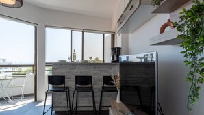 A modern kitchen with a bar area, large windows, and a view of the city. - Fiesta 1-Bedroom Apartment in Larnaca (Cyprus - Larnaca)