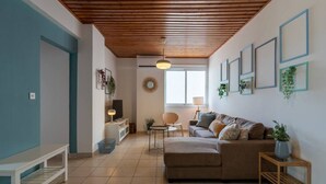 Ein Wohnzimmer mit Holzboden, einer Couch, einem Couchtisch und einem Fernseher. An der Wand hängen Bilder in Rahmen und auf dem Beistelltisch steht eine Pflanze.