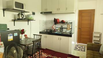 Una cocina compacta con microondas, estufa y lavaplatos, un comedor con mesa y sillas, y un sofá en la sala.