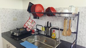 A kitchen with a gas stove, stainless steel sink, and a dish rack holding red plates and bowls.