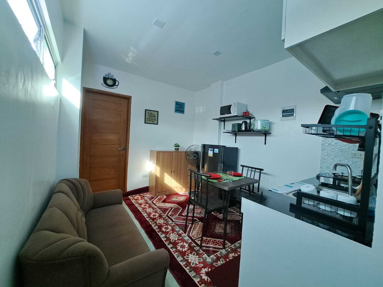 Un espace de vie compact comprenant un canapé, une table à manger avec des chaises, un réfrigérateur, un four à micro-ondes et un égouttoir à vaisselle.