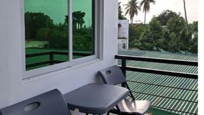 A balcony with two chairs and a table, a large window with a green view, and a metal railing.