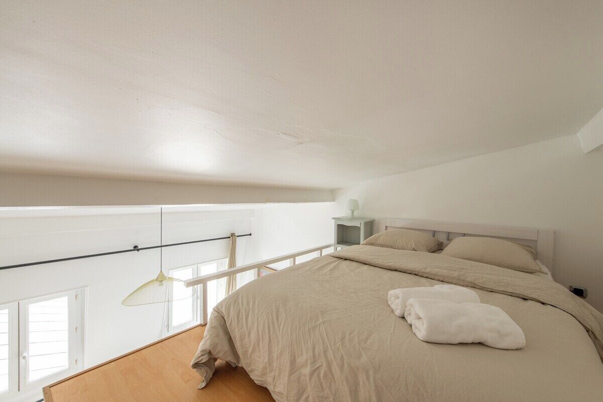 Ein Schlafzimmer mit einem großen Bett, einem Nachttisch, einer Pendelleuchte und Blick ins Freie durch ein Fenster.