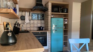 A kitchen with a stone wall, wooden countertop, black kettle, stove, blue refrigerator, and a blue chair.