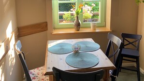 A dining area with a table set for four, a window with a view of greenery, and a hanging light fixture.