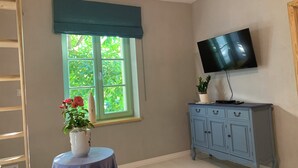 A room with a window, a television mounted on the wall, a cabinet, and a small table with a vase of flowers.