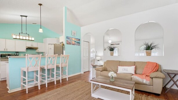 A living room with a beige sofa, a coffee table, and a dining area with a white table and chairs. - Pelican Palm - Poolside holiday escape! (Palm Coast)