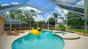 A covered swimming pool with a slide, lounge chairs, and a rubber duck float. - Pelican Palm - Poolside holiday escape! (Palm Coast)