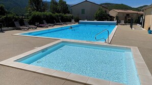 A rectangular pool with a diving board, surrounded by lounge chairs and a building with a tiled roof. - Logement 2 Chambres, Entièrement Rénové, Dans Résidence Avec Piscine (Montbrun-les-Bains)