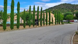 A road lined with tall cypress trees, a sign reading "Bienvenue Welcome Le Domaine Les Sources," and a building in the background. - Logement 2 Chambres, Entièrement Rénové, Dans Résidence Avec Piscine (Montbrun-les-Bains)