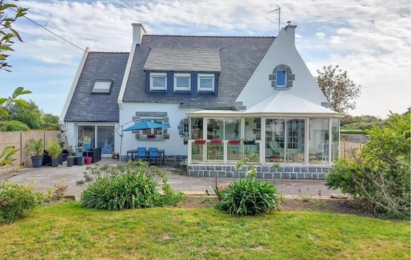 A two-story house with a conservatory, a patio with outdoor furniture, and a garden.