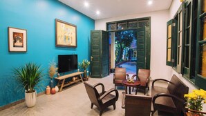 Ein Wohnzimmer mit blauer Wand, Deckenventilator, Fernseher und Blick auf einen Garten durch eine offene Tür.