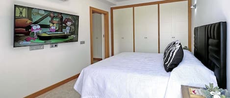 Un dormitorio con cama, televisor montado en la pared, armario y una mesita con una planta.