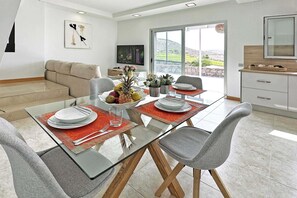 A modern dining area with a glass table, grey chairs, and a red placemat.