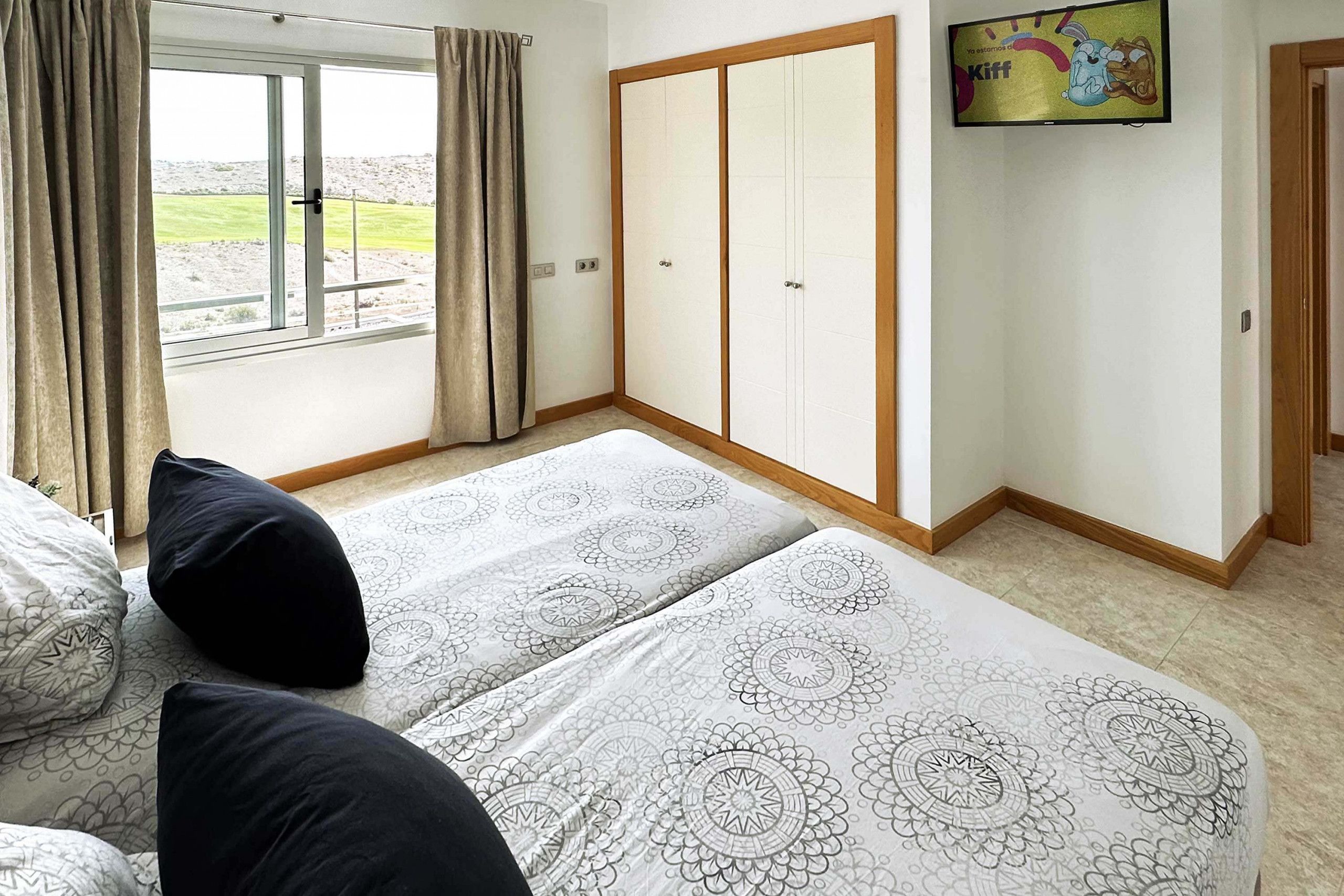 A bedroom with two beds, a sliding door closet, and a TV on the wall.