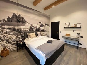 Un dormitorio moderno con una cama grande, un escritorio y un mural en la pared con un paisaje montañoso.