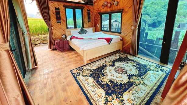 A wooden room with a bed, a large window, and a view of greenery outside. - Thóc house (Ta Van)