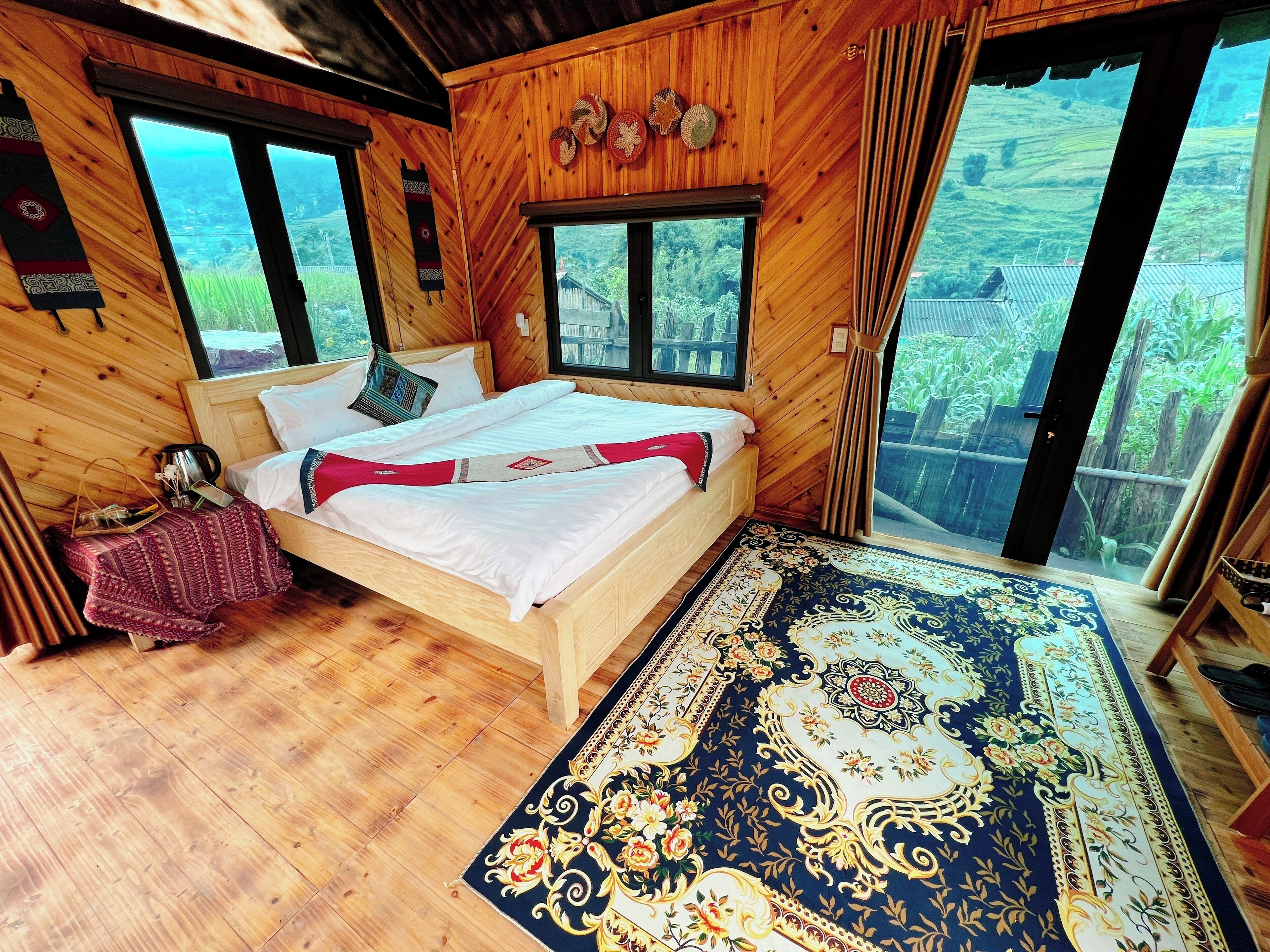 A wooden room with a bed, a small table, and a large window.