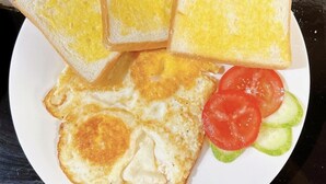 A plate with two fried eggs, two slices of toast, and a side of sliced tomatoes and cucumbers. - Thóc house (Ta Van)