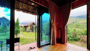 A room with large glass doors leading to an outdoor area with a view of a rural landscape and a wooden structure. - Thóc house (Ta Van)