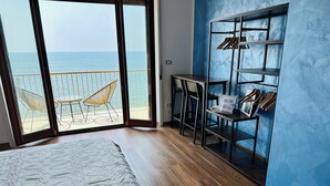 A bedroom with a large bed, a wooden floor, a blue wall, a metal wardrobe, and a view of the sea. - BluMare ArtHouse (Salerno)