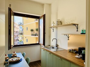 Een kleine keuken met een raam, een spoelbak en een eethoek met een tafel en stoelen.