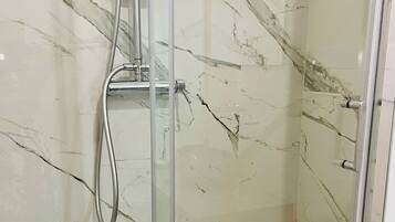 A glass-enclosed shower with a chrome faucet and handheld showerhead, marble-patterned walls, and a tiled floor.
