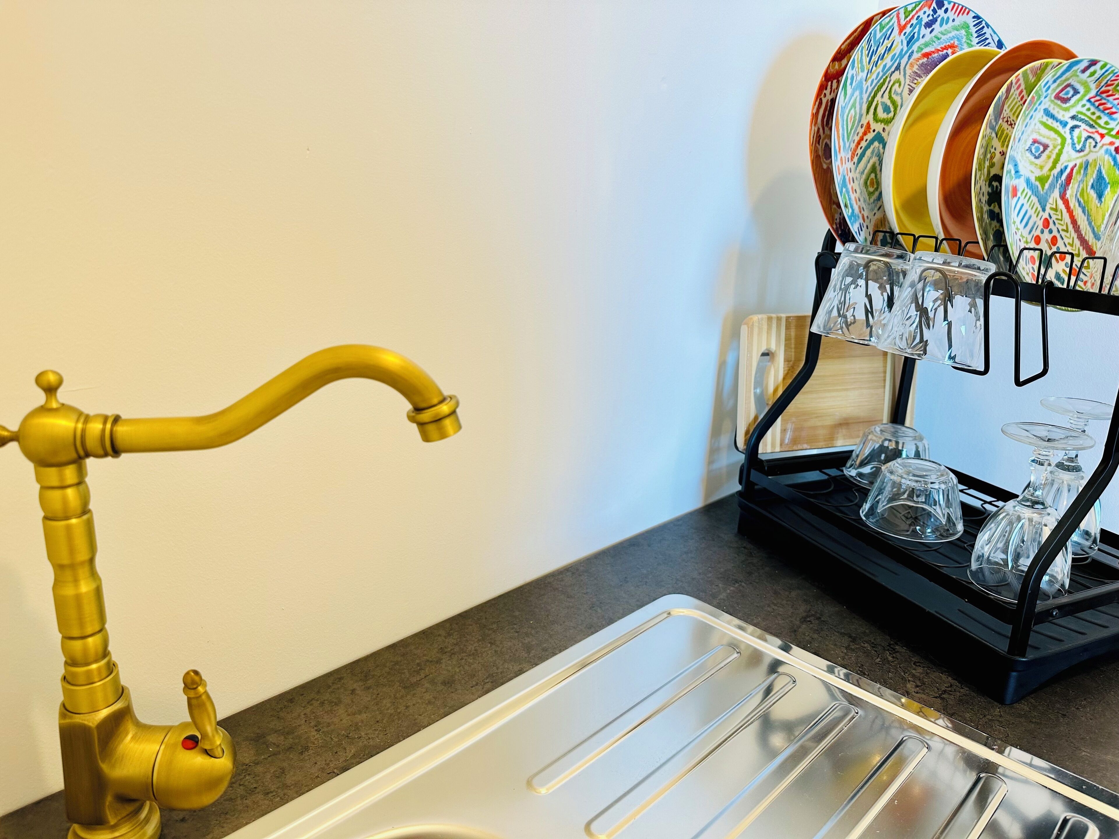 Un lavamanos de cocina con grifo dorado y un escurreplatos con platos y vasos de colores.