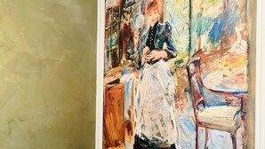 A room with a large painting on the wall, a light blue sofa, and a wooden chair. - BluMare ArtHouse (Salerno)