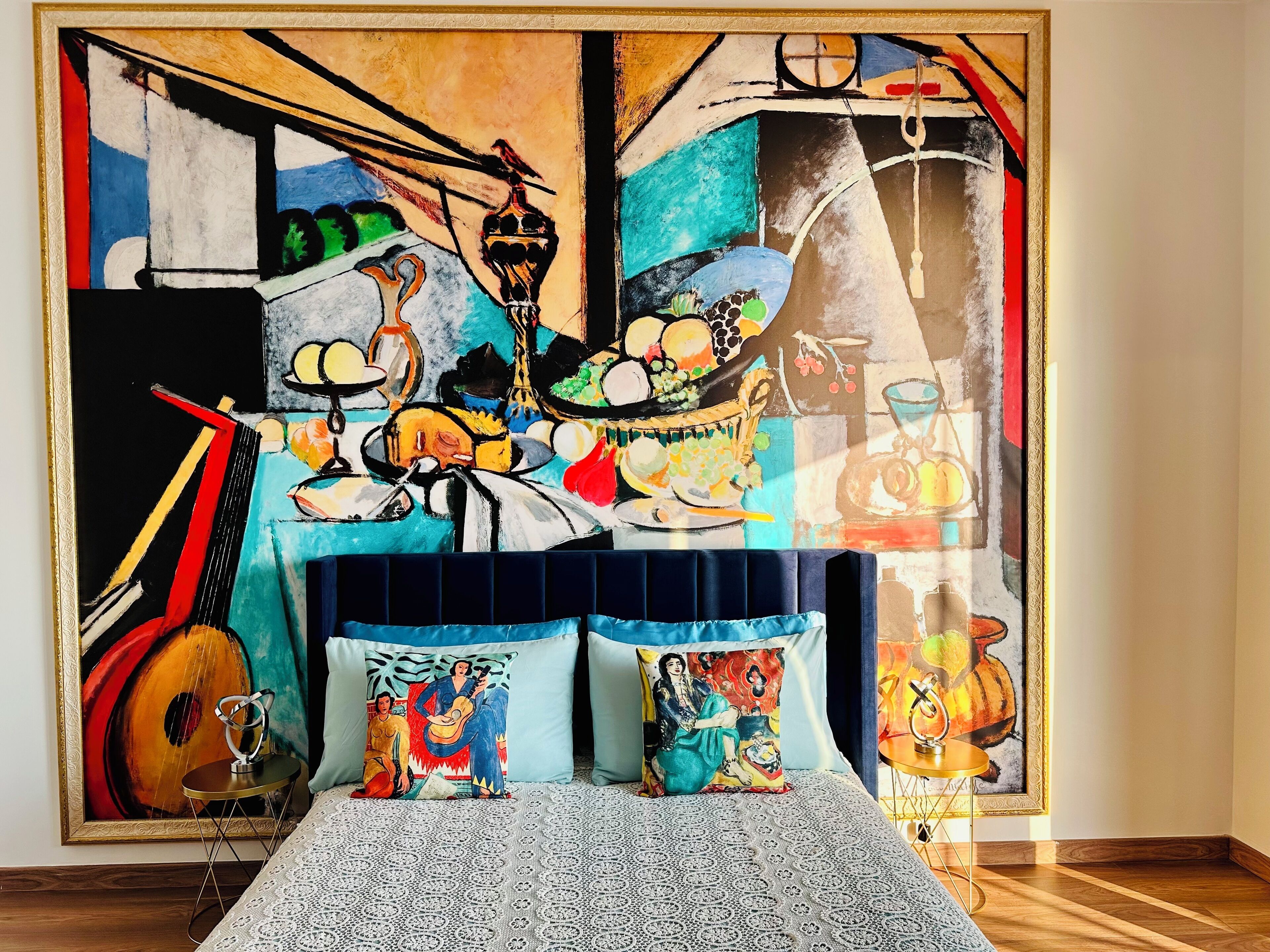 Una habitación con una cama, un cuadro grande en la pared y una mesita con una guitarra.
