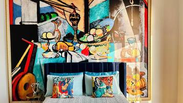 Una habitación con una cama, un cuadro grande en la pared y una mesita con una guitarra.