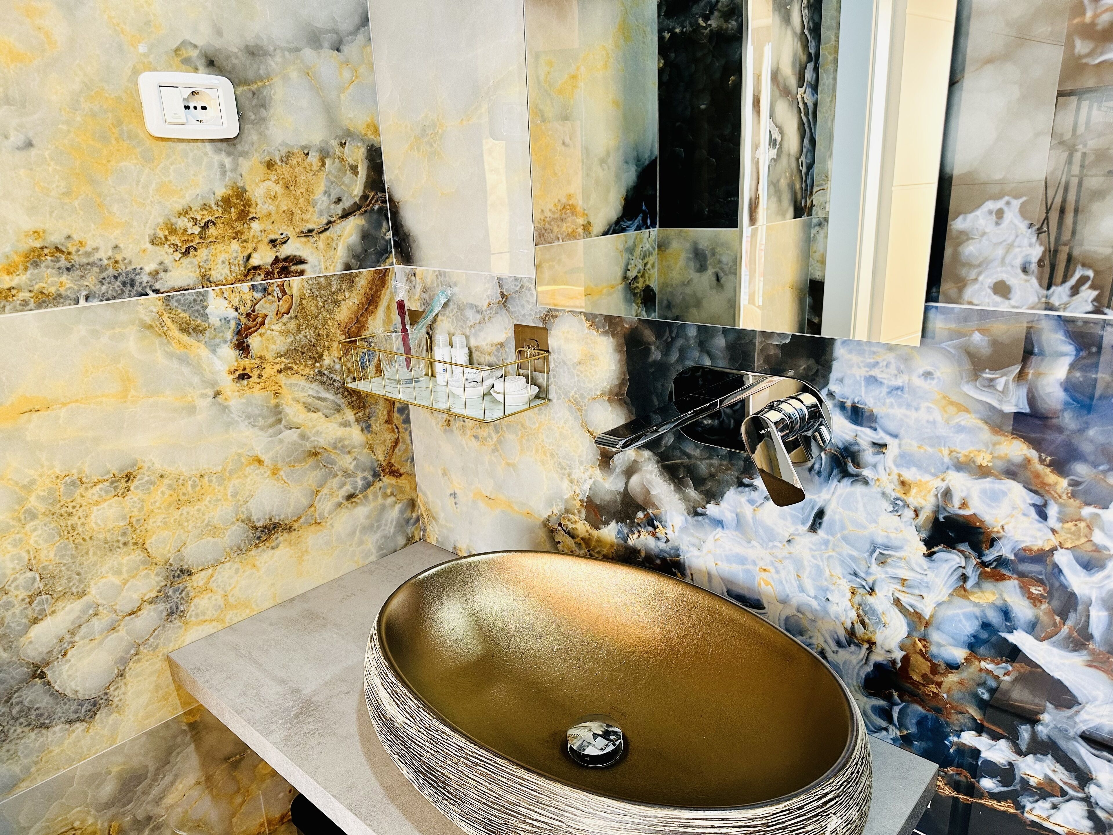 A bathroom with a marble vanity, a gold sink, and a mirror.