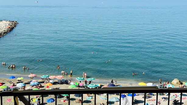 A beach with people swimming and sunbathing, umbrellas, and a rocky breakwater. - BluMare ArtHouse (Salerno)