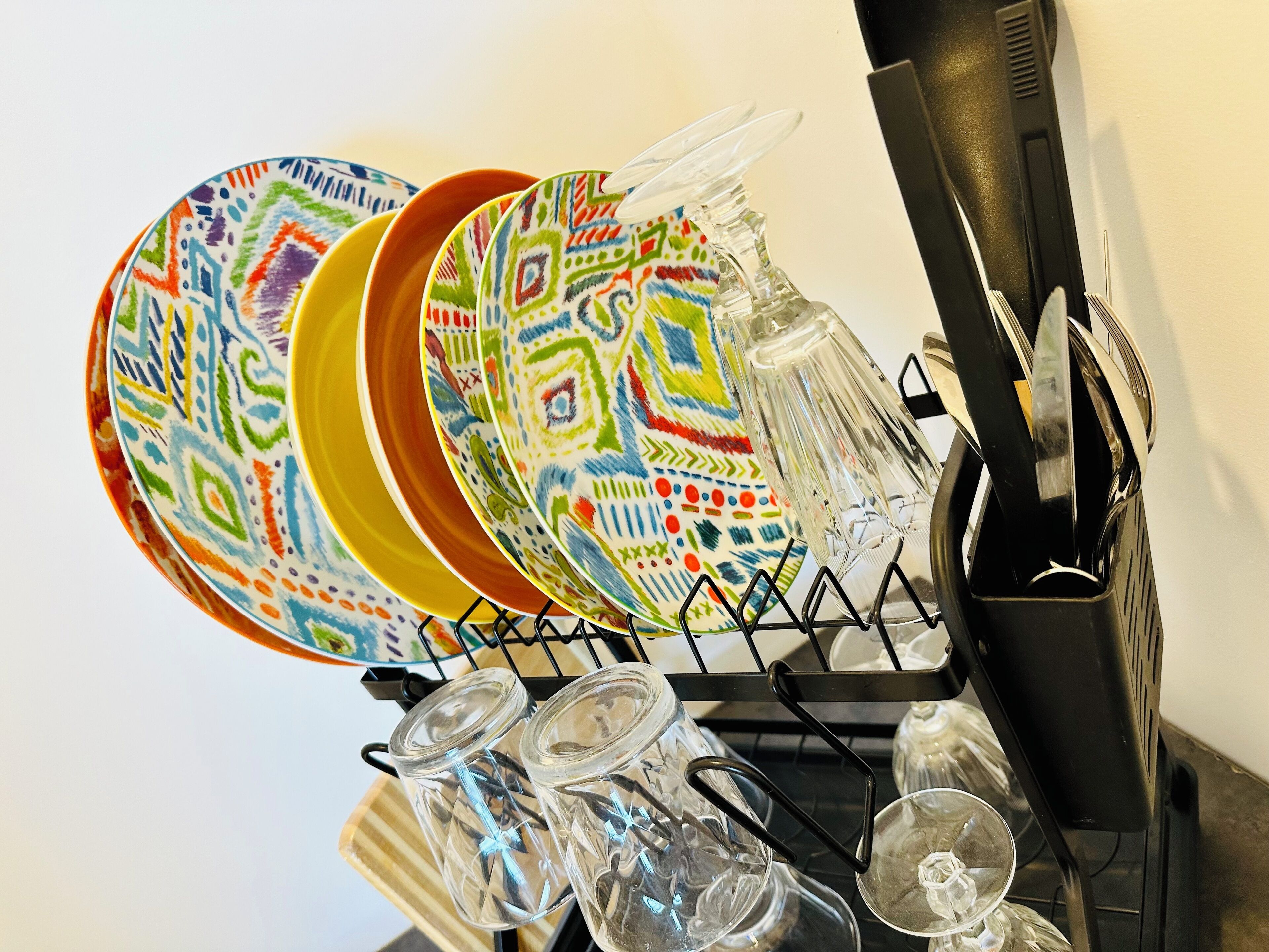 A dish rack with colorful plates, a glass pitcher, and clear glassware.