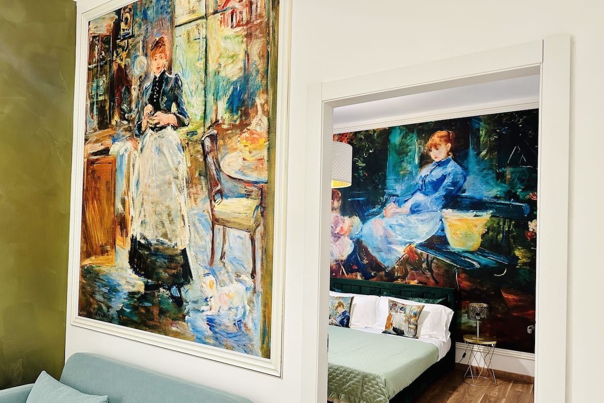 A room with a bed, a blue sofa, and two paintings on the wall.