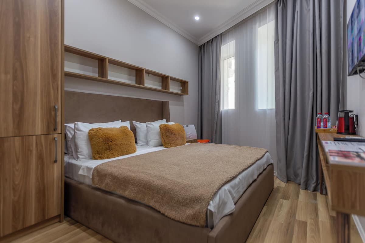 Un dormitorio con cama, cabecero de madera, un escritorio con silla y televisor en la pared.
