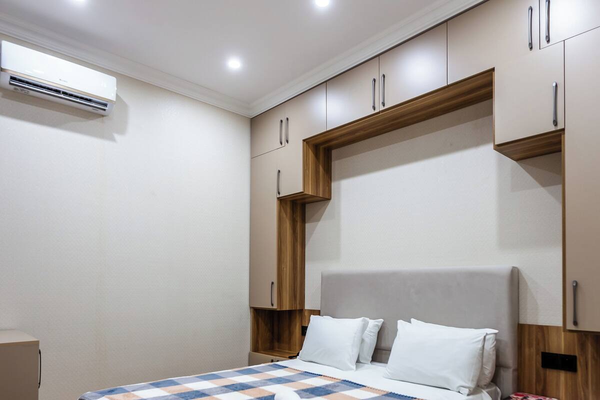 Una habitación de hotel moderna con una cama grande, suelo de madera, armario empotrado y aire acondicionado.