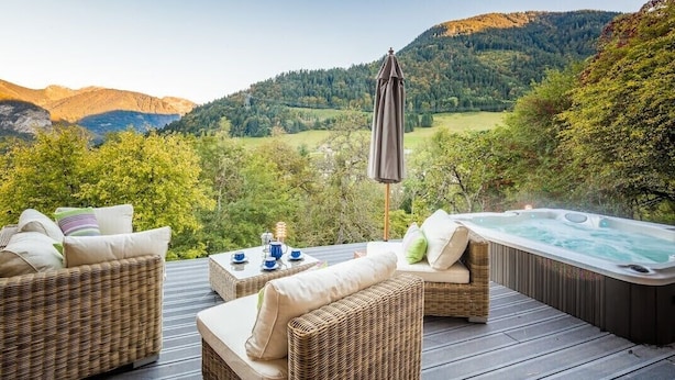 Eine Terrass mit Korbmöbeln, einem Whirlpool und einem schönen Blick auf Hügel und Bäume.