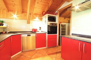 A kitchen with red cabinets, stainless steel appliances, and wooden ceiling beams.
