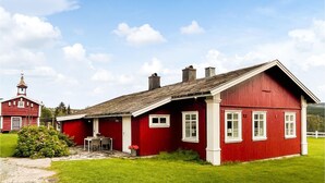 Ein rotes Holzhaus mit weißer Tür, einer kleinen Veranda und einem Steinweg, der davor führt.