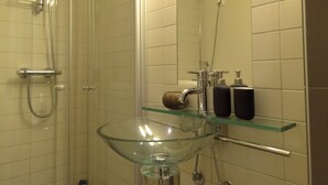 Un baño con lavamanos de vidrio, ducha y espejo.