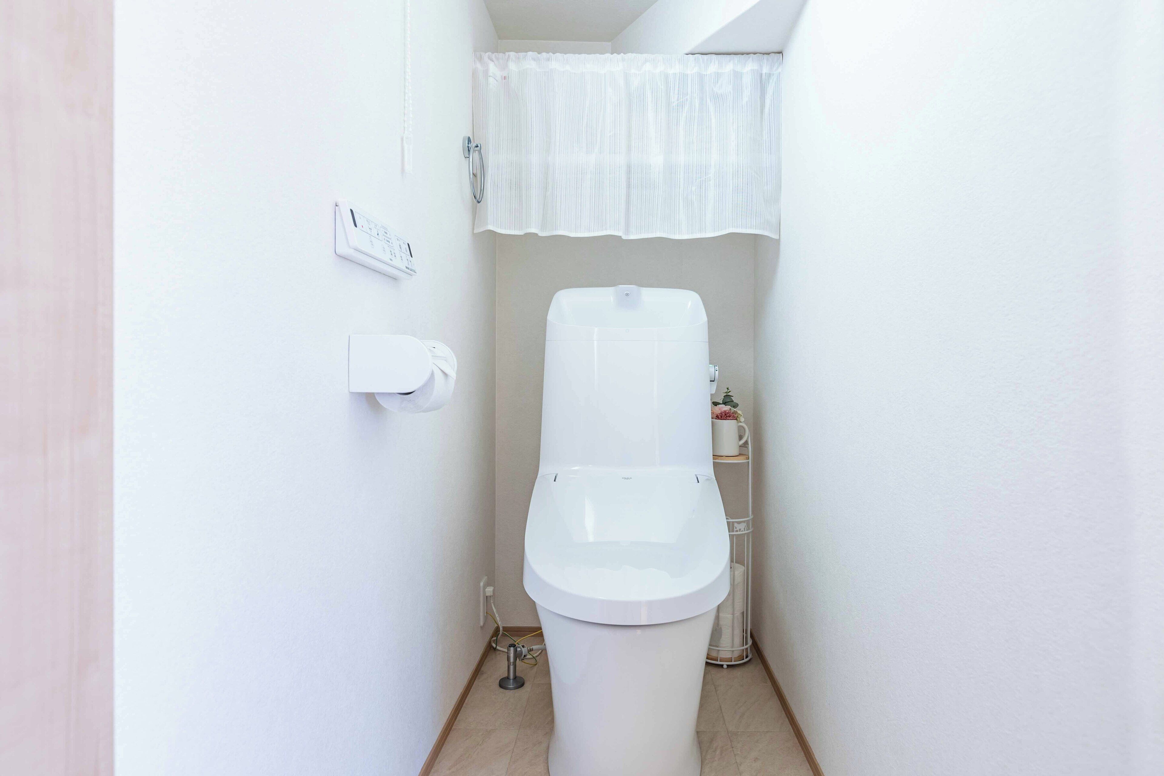 Un baño pequeño y blanco con inodoro, dispensador de papel higiénico y cortina de ducha.