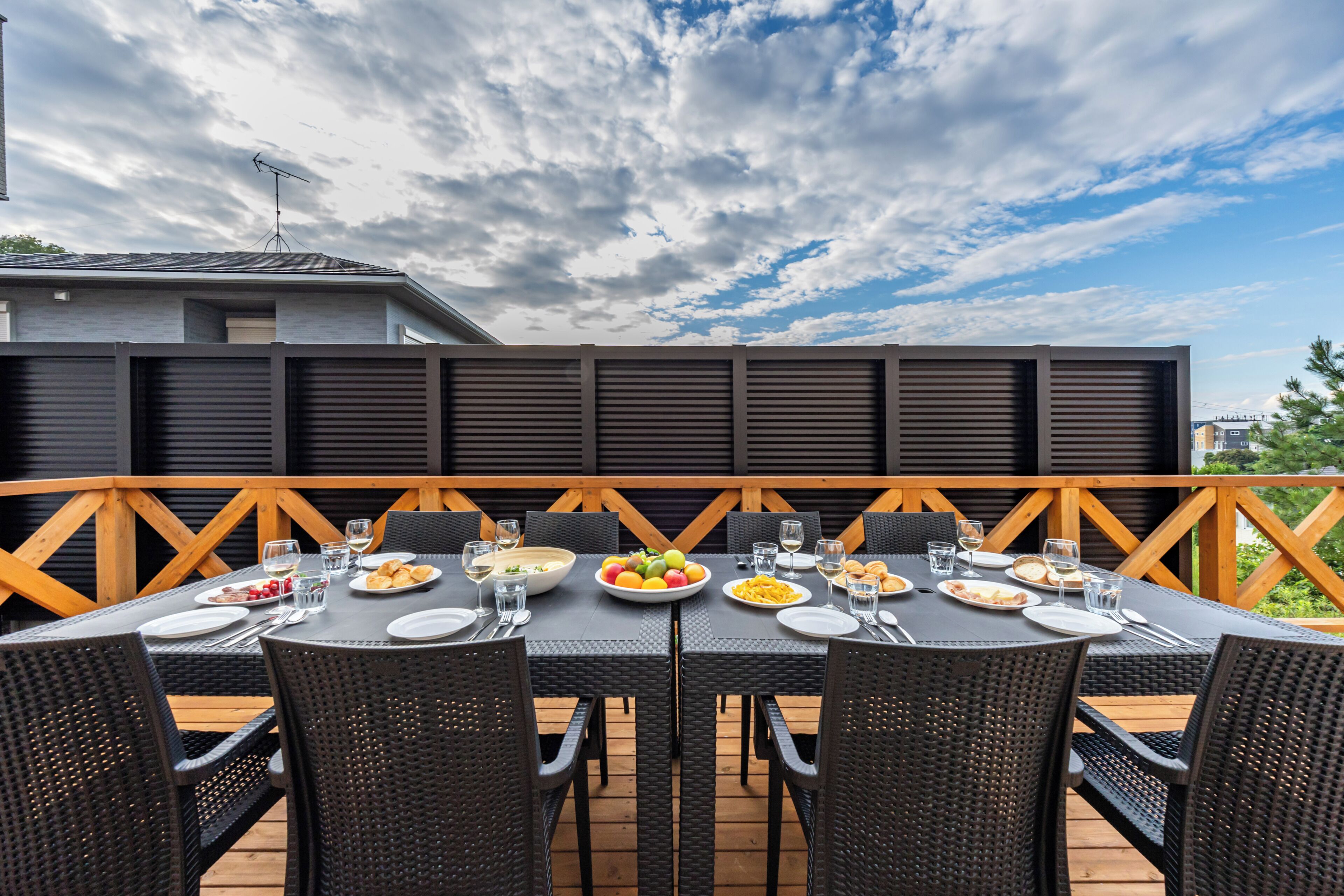 Un área de comedor al aire libre con terraza de madera, mobiliario de ratán negro y diversos platos y vasos sobre las mesas.