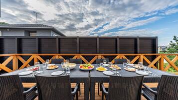Un área de comedor al aire libre con terraza de madera, mobiliario de ratán negro y diversos platos y vasos sobre las mesas.