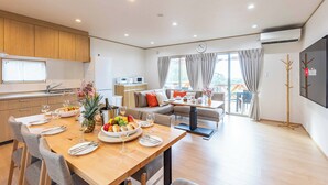A modern kitchen with wooden cabinets, a dining area with a wooden table set for a meal, and a living area with a sofa and a TV. - PEACE OF REST  SHIRAHAMA (Shirahama)